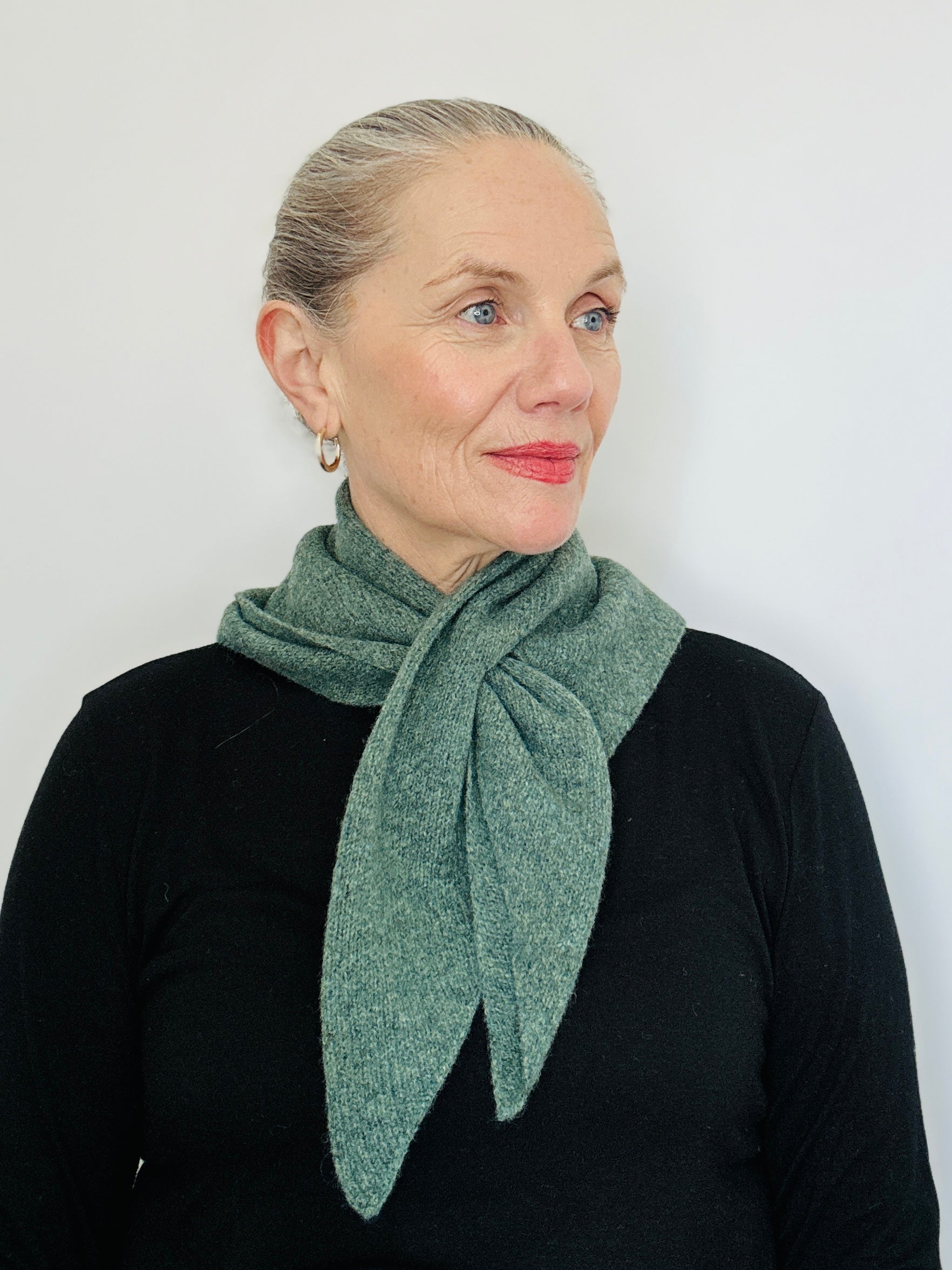 Beautiful sexy woman in a black top, with lipstick on and her hair tied back wearing merino lambswool double layer solid colour, peacock green pull through triangle scarf / kerchief / neckerchief for women, men, unisex in a black top.