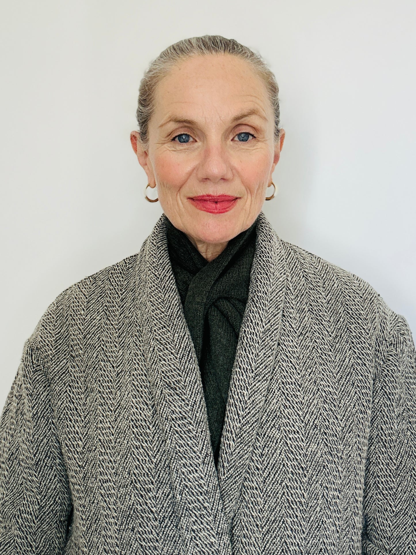 Beautiful sexy woman with a grey coat on and her hair tied back wearing a merino lambswool double layer solid colour, olive green pull through triangle scarf / kerchief / neckerchief for women, men, unisex against a neutral backdrop