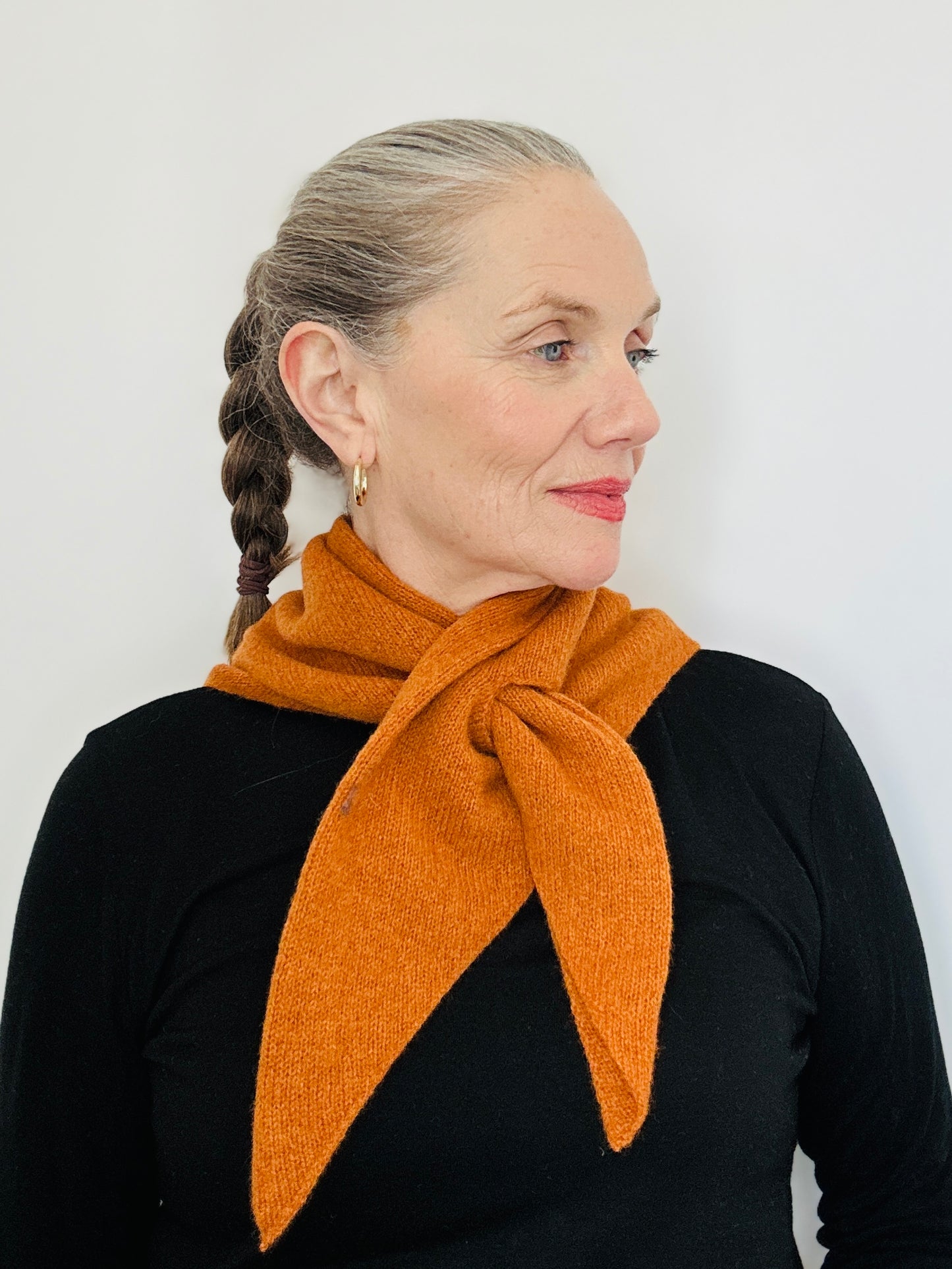 Beautiful sexy woman in a black top wearing merino lambswool double layer solid colour, rust pull through triangle scarf / kerchief / neckerchief for women, men, unisex on a neutral background