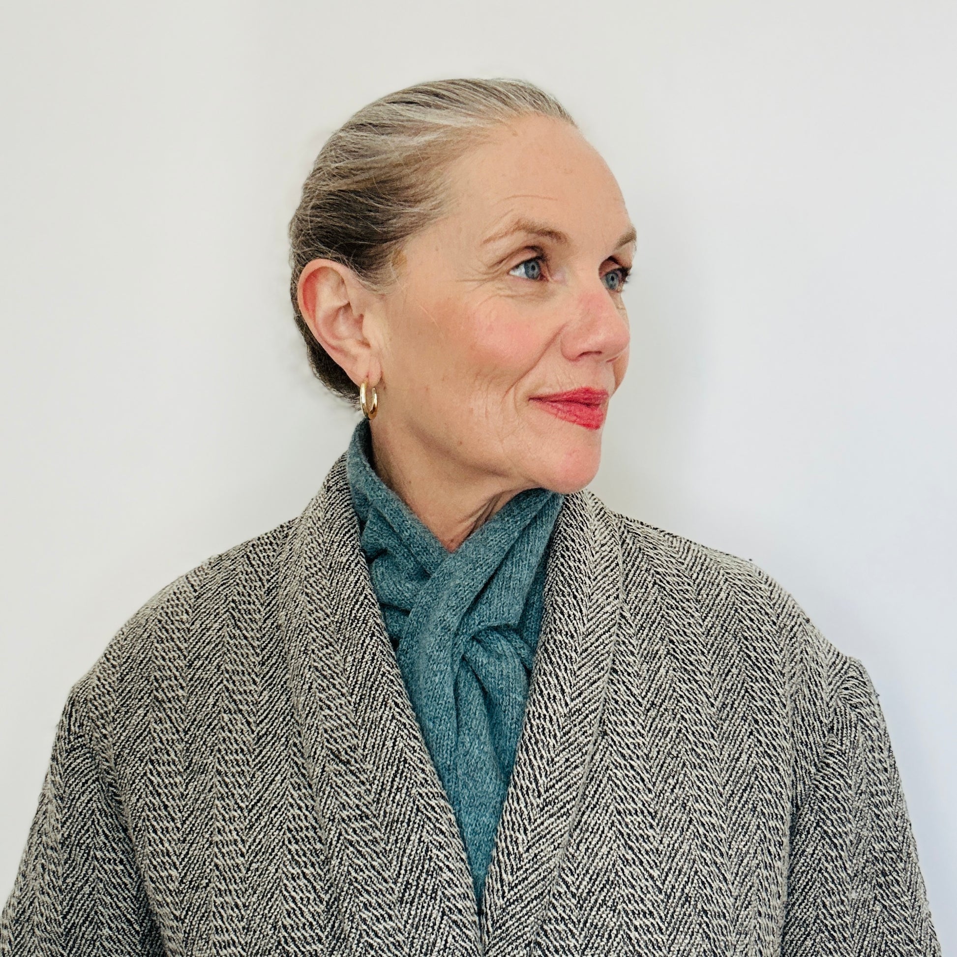 Beautiul sexy woman with a grey coat on, wearing merino lambswool double layer solid colour, caspian blue pull through triangle scarf / kerchief / neckerchief for women, men, unisex against white backing