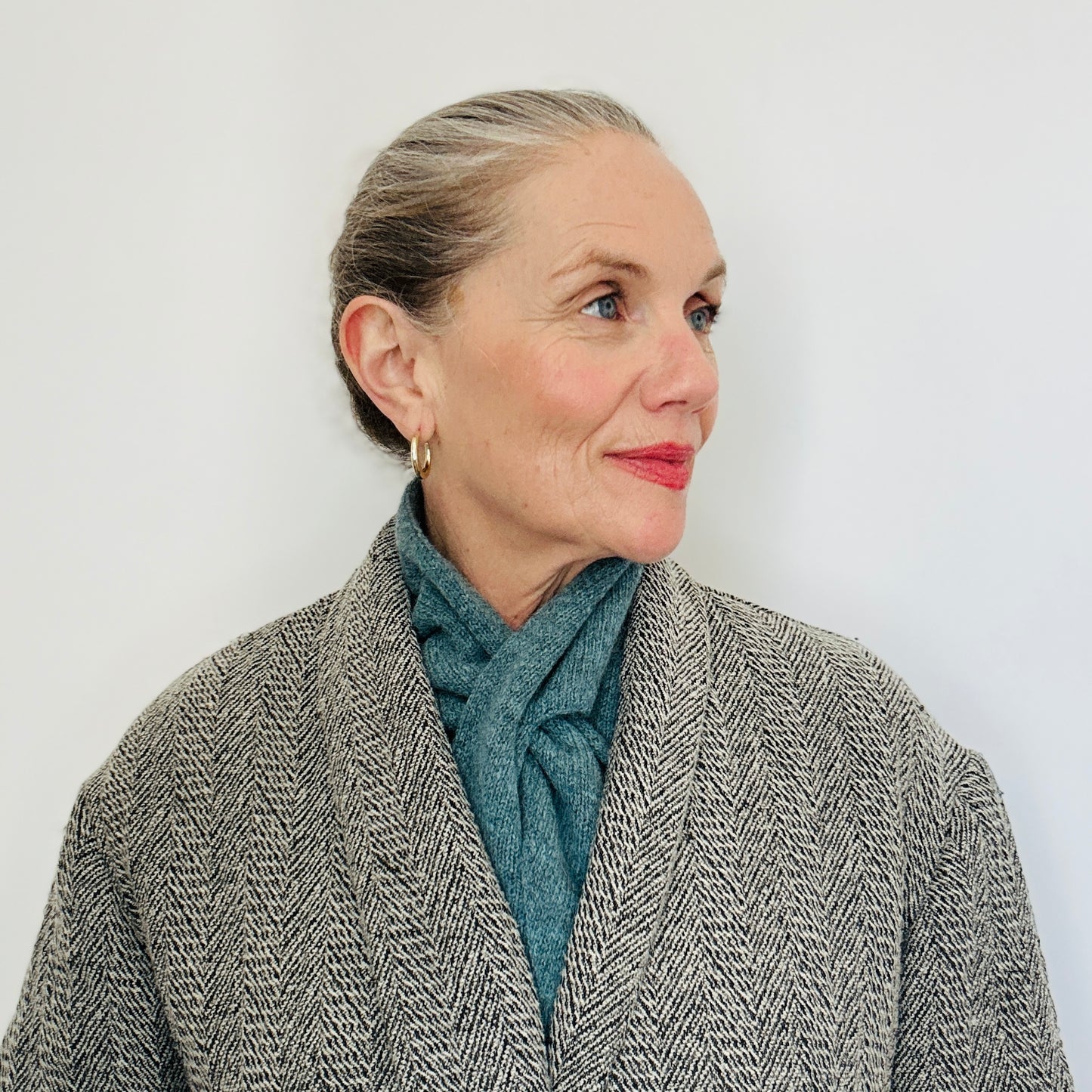 Beautiul sexy woman with a grey coat on, wearing merino lambswool double layer solid colour, caspian blue pull through triangle scarf / kerchief / neckerchief for women, men, unisex against white backing