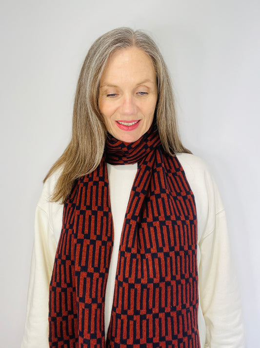 Beautiful sexy woman in a white top wearing a Brown Sienna and Navy handcrafted merino Lambswool Geometric patterned Scarf on a neutral background Pom Shanty Knitwear