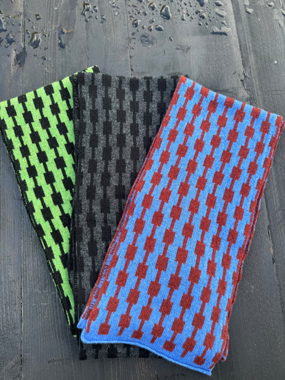 Three different coloured hand crafted merino lambswool geometric patterned Pulse scarves fanned out on a grey wooden table.
