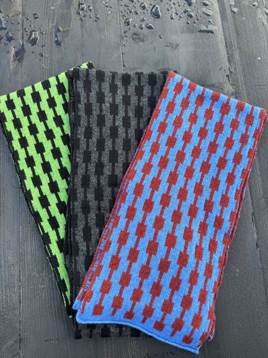 Three different coloured hand crafted merino lambswool geometric patterned Pulse scarves fanned out on a grey wooden table.