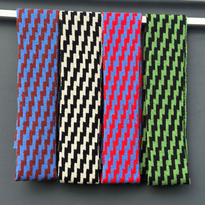 Four rick rack geometric patterned merino lambswool skinny scarves hanging on a rod against a gray background